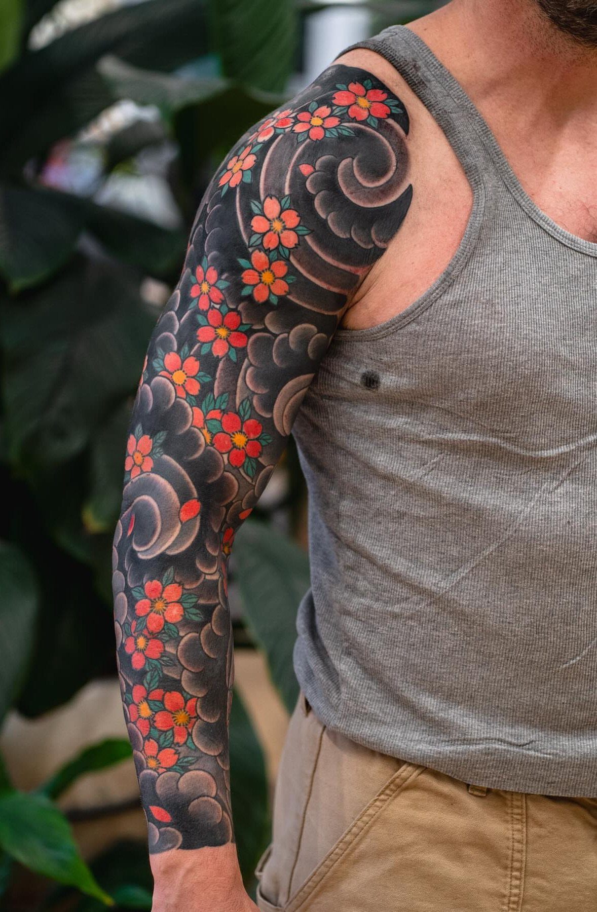 Man's arm with a Japanese sleeve tattoo of dark clouds and red cherry blossoms.