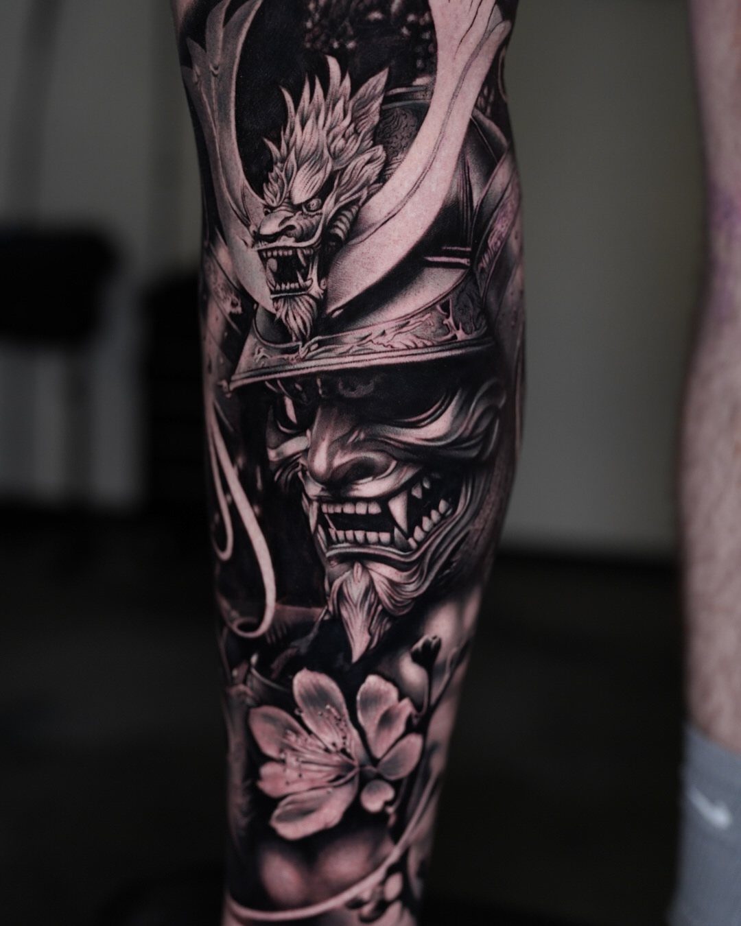 Demonic face tattoo with samurai helmet and cherry blossom on a man's arm