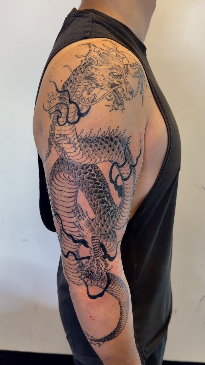 Japanese dragon tattoo in black ink on a man's upper arm and shoulder.
