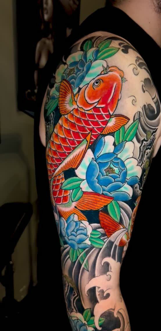 Orange koi fish tattoo with blue peonies and waves on a man's arm
