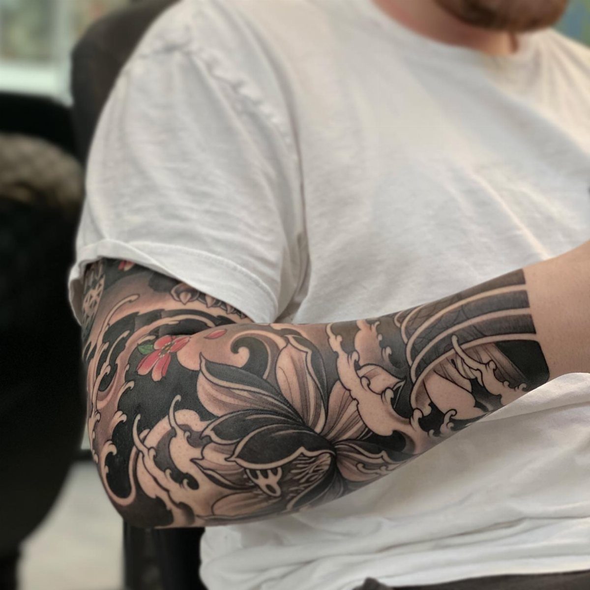 Japanese tattoo sleeve on a man's arm featuring a large lotus flower and waves.