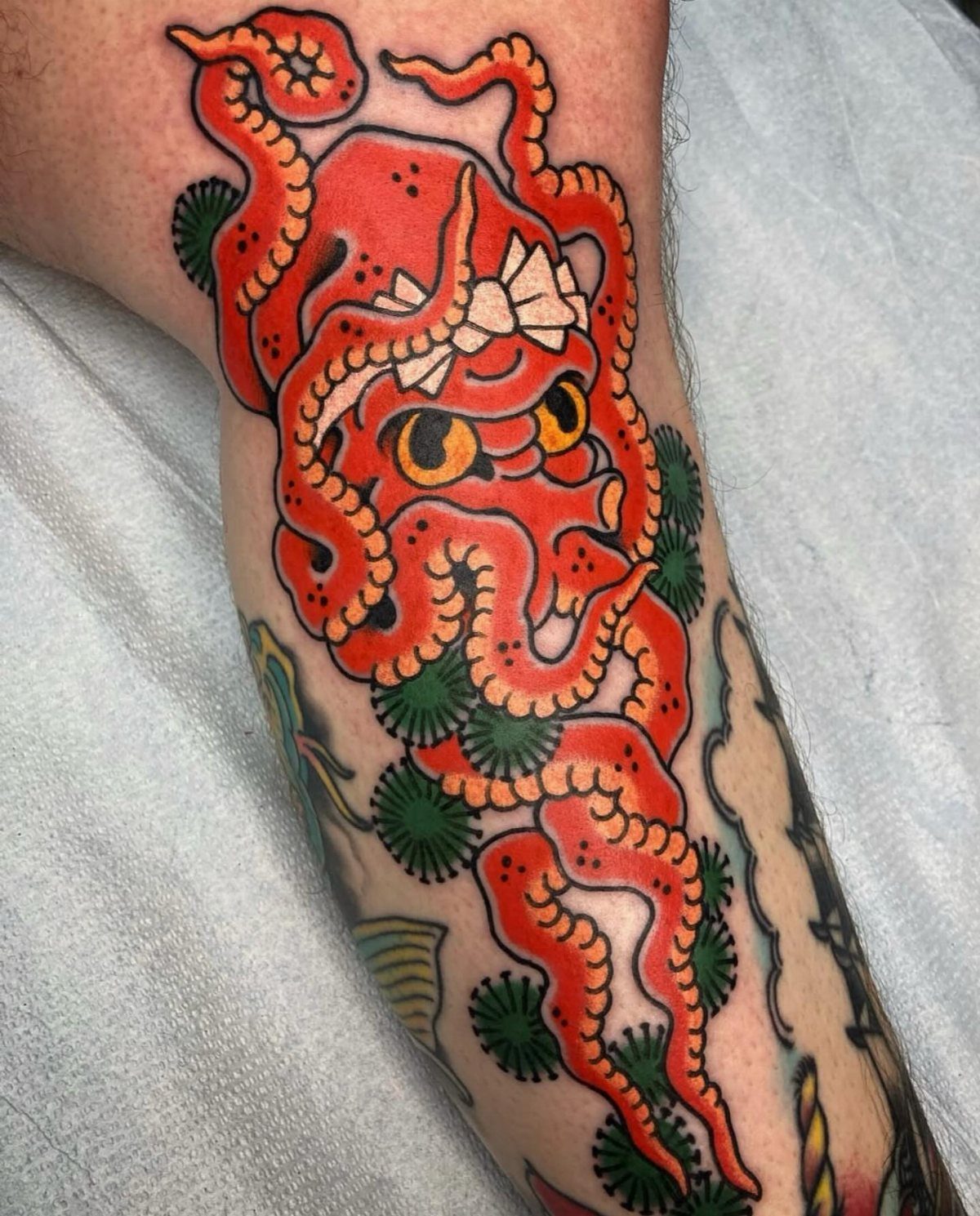 Red octopus tattoo with yellow eyes on a person's leg with green accents.