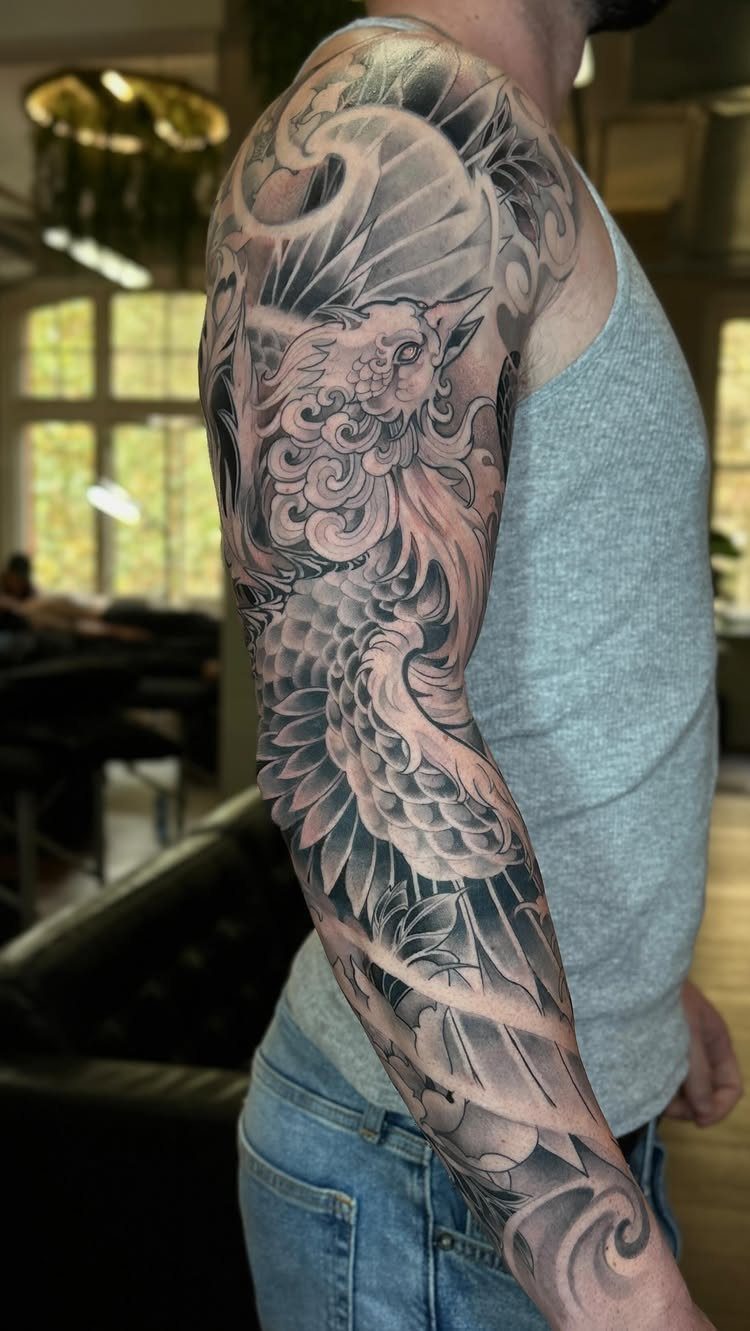 Detailed black and grey Japanese phoenix tattoo covering a man's shoulder and arm.