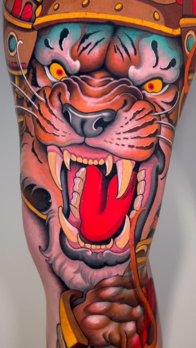Tiger head tattoo with open mouth and yellow eyes on human skin.
