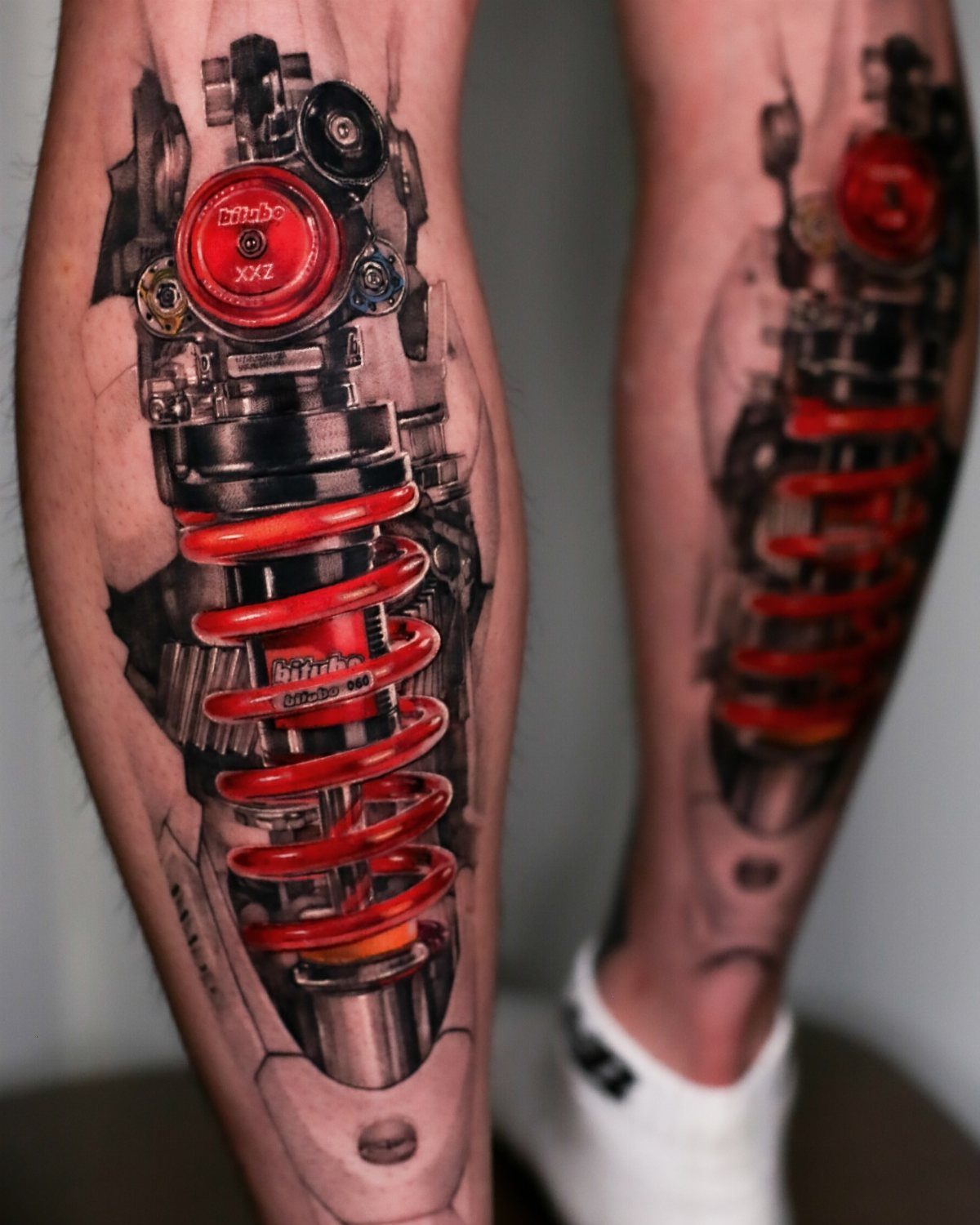 Biomechanical leg tattoo featuring a red mechanical spring and metallic parts under the skin.