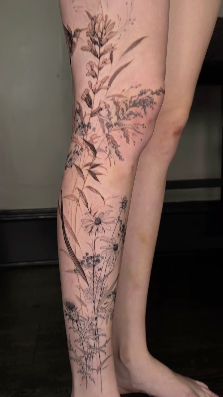 Botanical leg tattoo with fine line wildflowers and grasses on a person's leg.