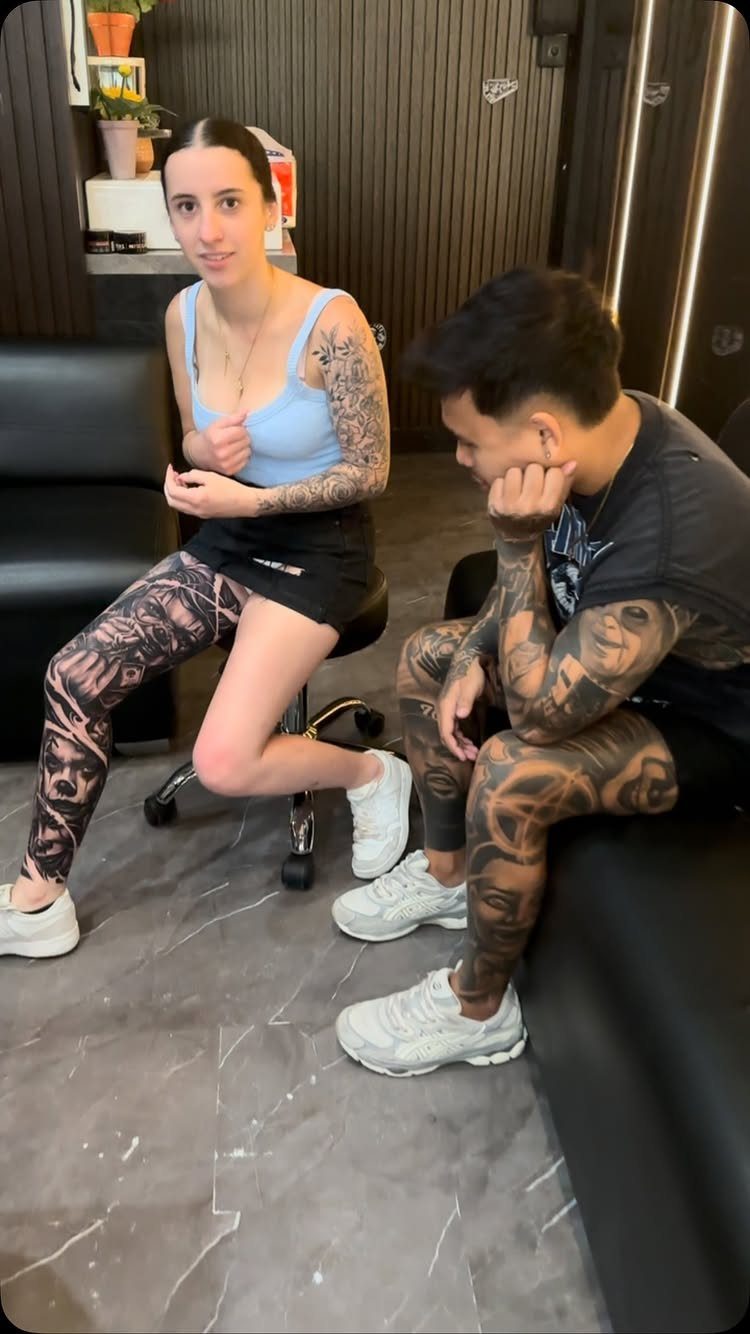 Man and woman with full leg sleeve tattoos sitting in a studio.