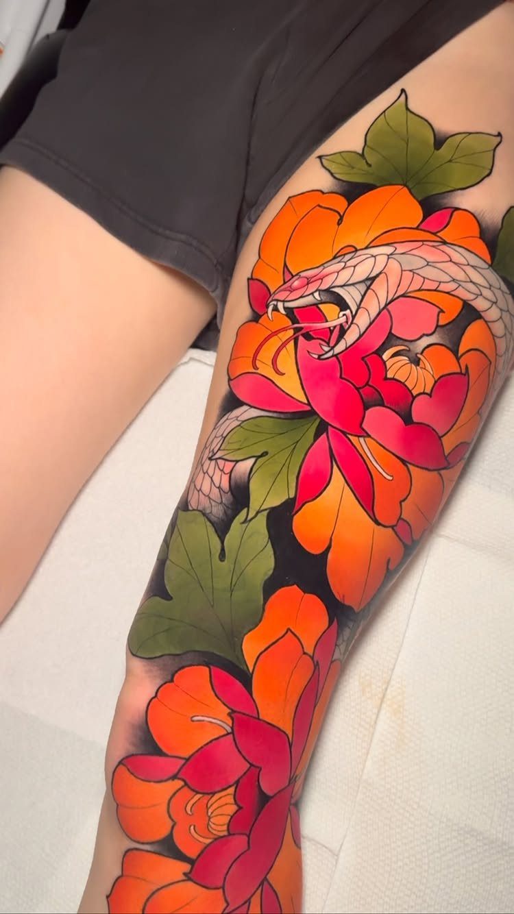 Snake tattoo weaving through orange and red peony flowers on a person's leg