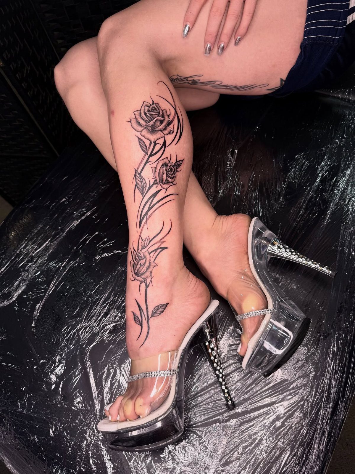 Black rose tattoo on a woman's lower leg wearing clear platform high heels.