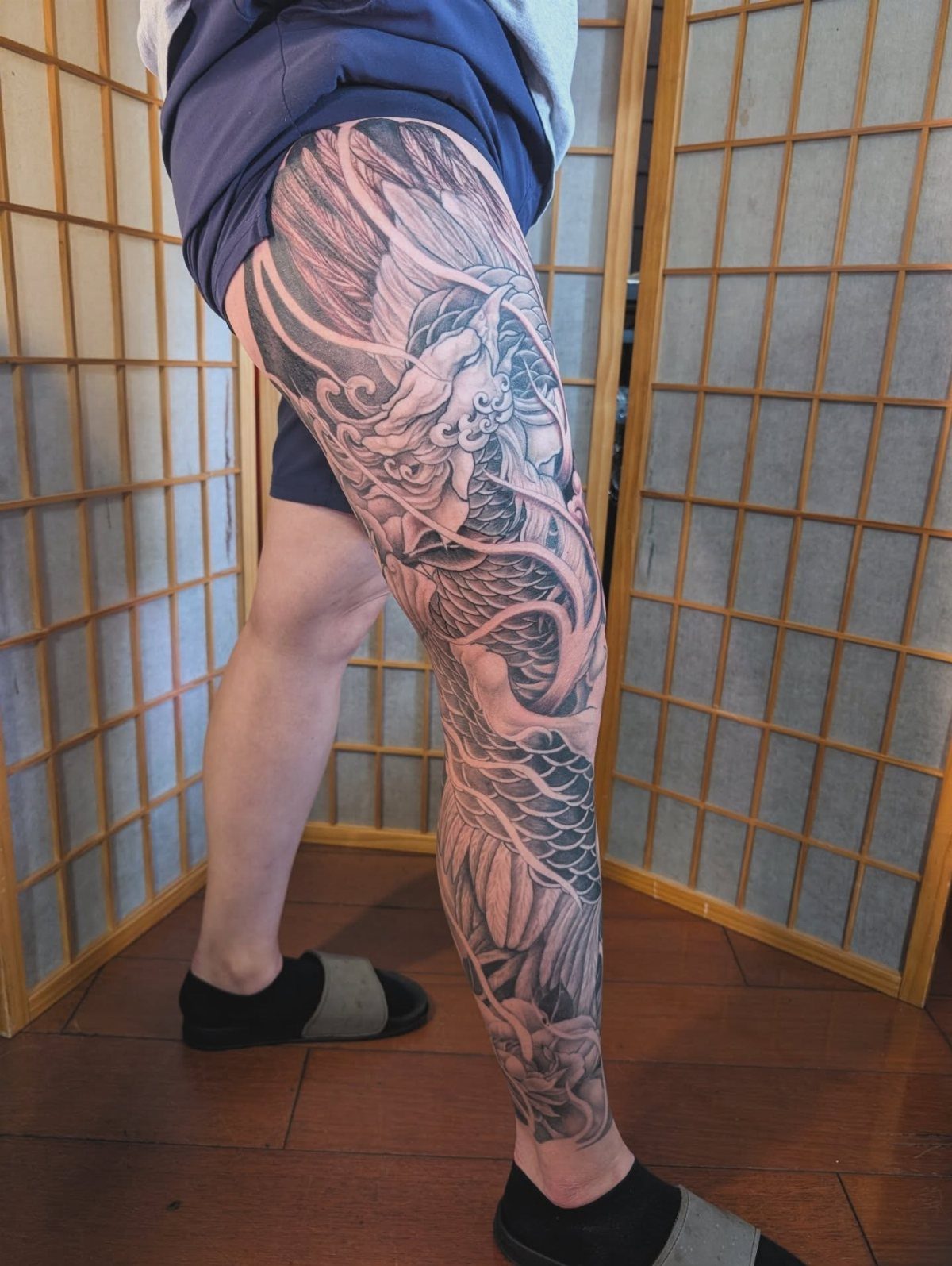 Full leg sleeve tattoo with a black and grey dragon and floral design.