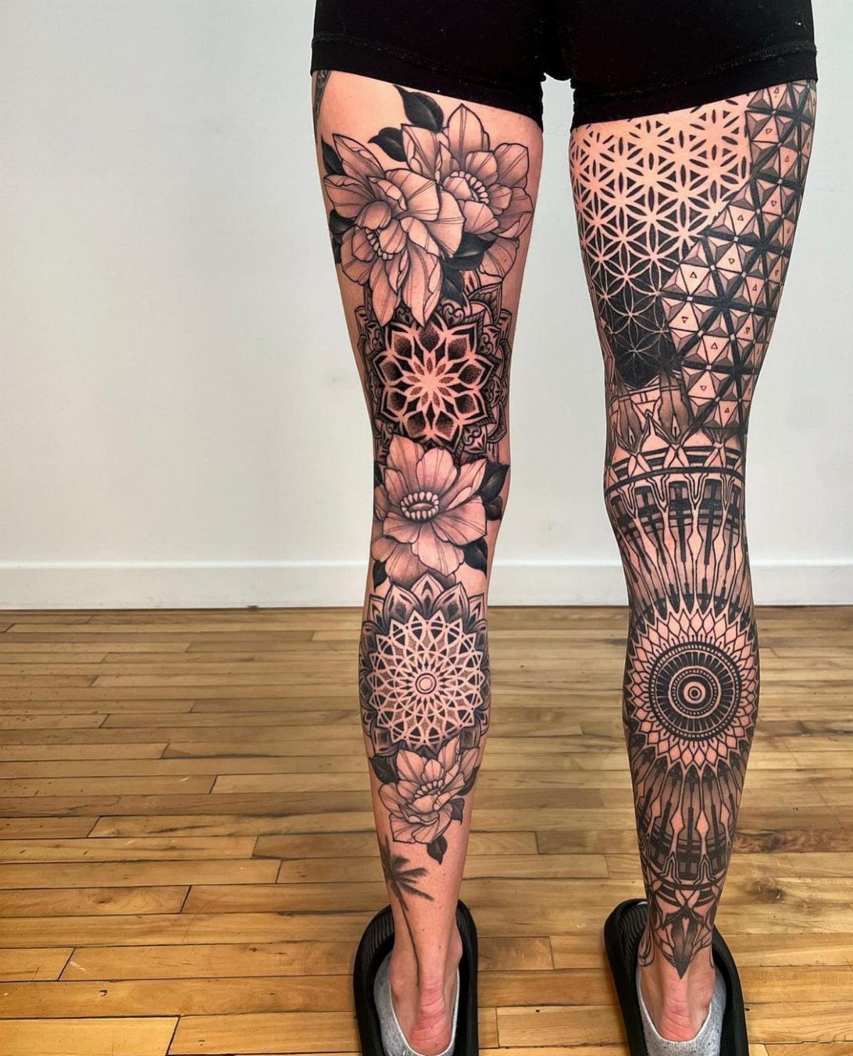 Legs with intricate black ink geometric and floral tattoos on a wooden floor