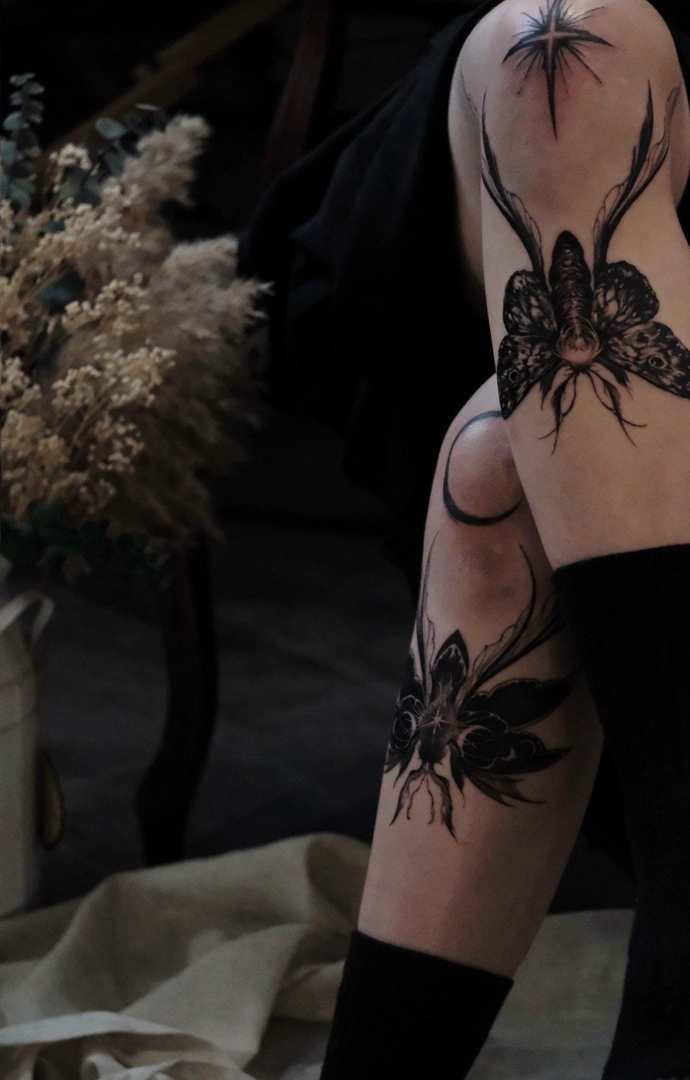Legs with black ink tattoos including a moth on the knee and floral designs.