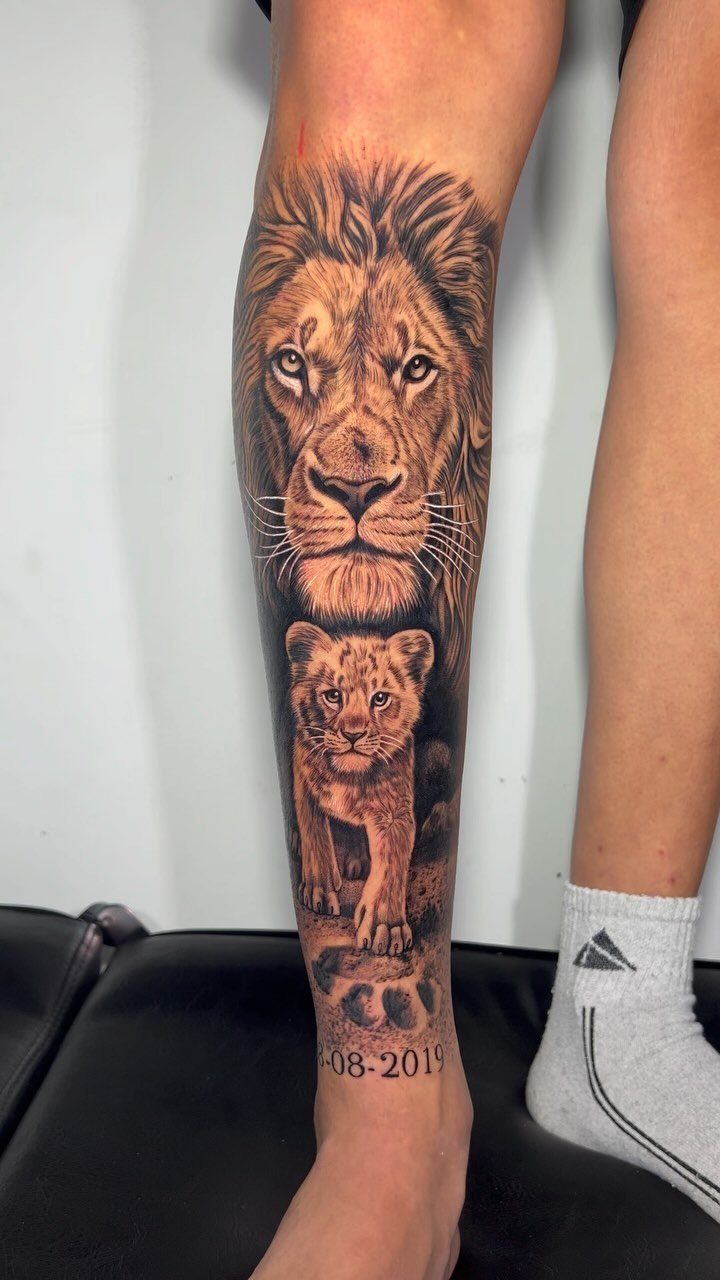 Realistic lion and lion cub tattoo on a person's lower leg.