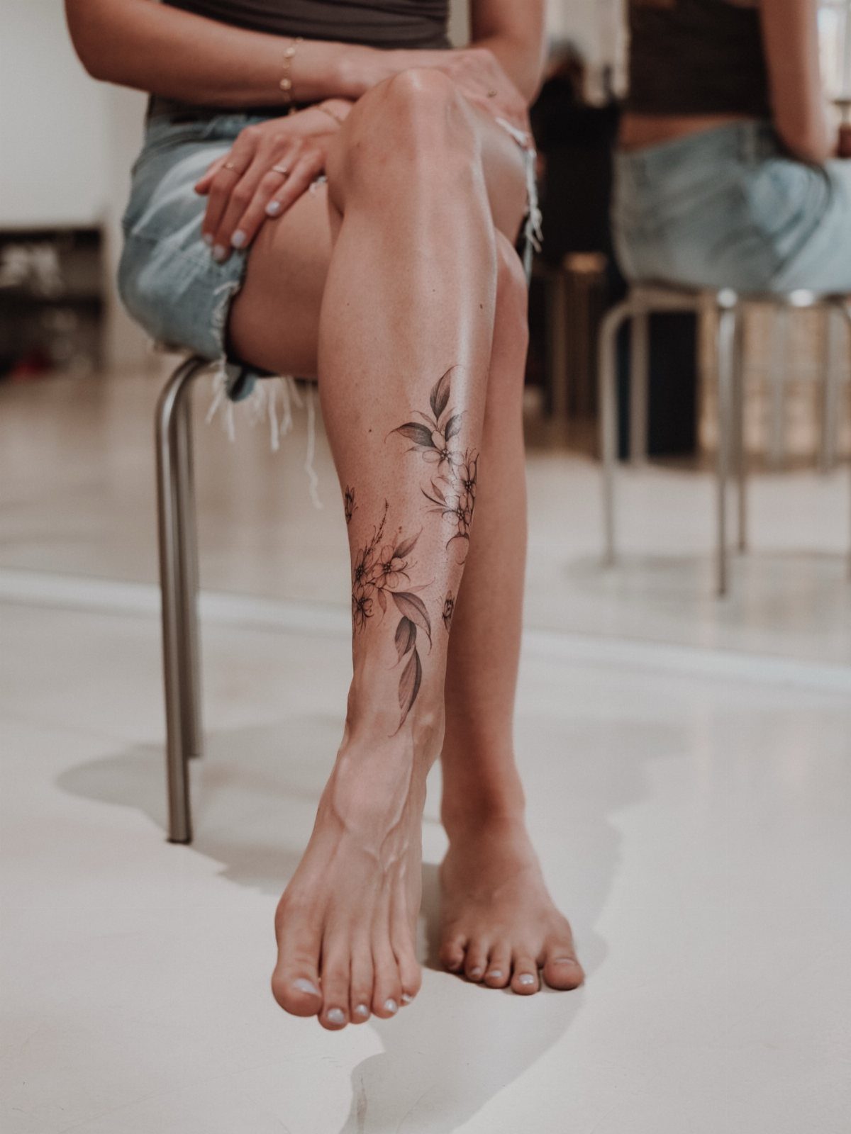 Woman's lower leg with a minimalist black ink floral and leaf tattoo.