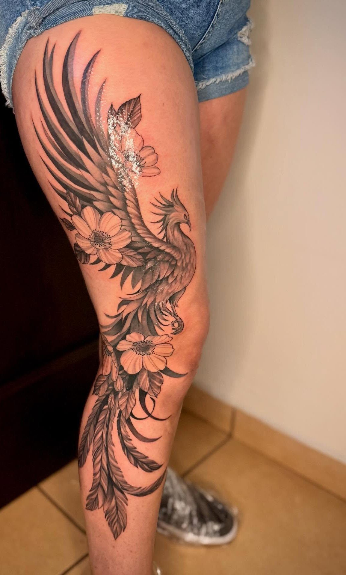 Phoenix and flower tattoo in black ink covering a woman's leg from thigh to shin.