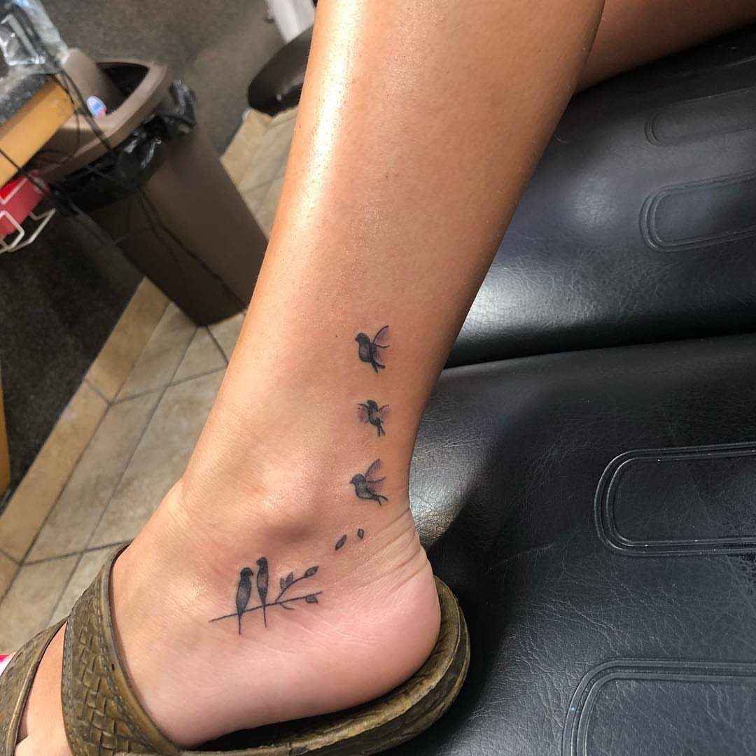 Small black bird tattoos on a woman's ankle, including birds perched on a branch.