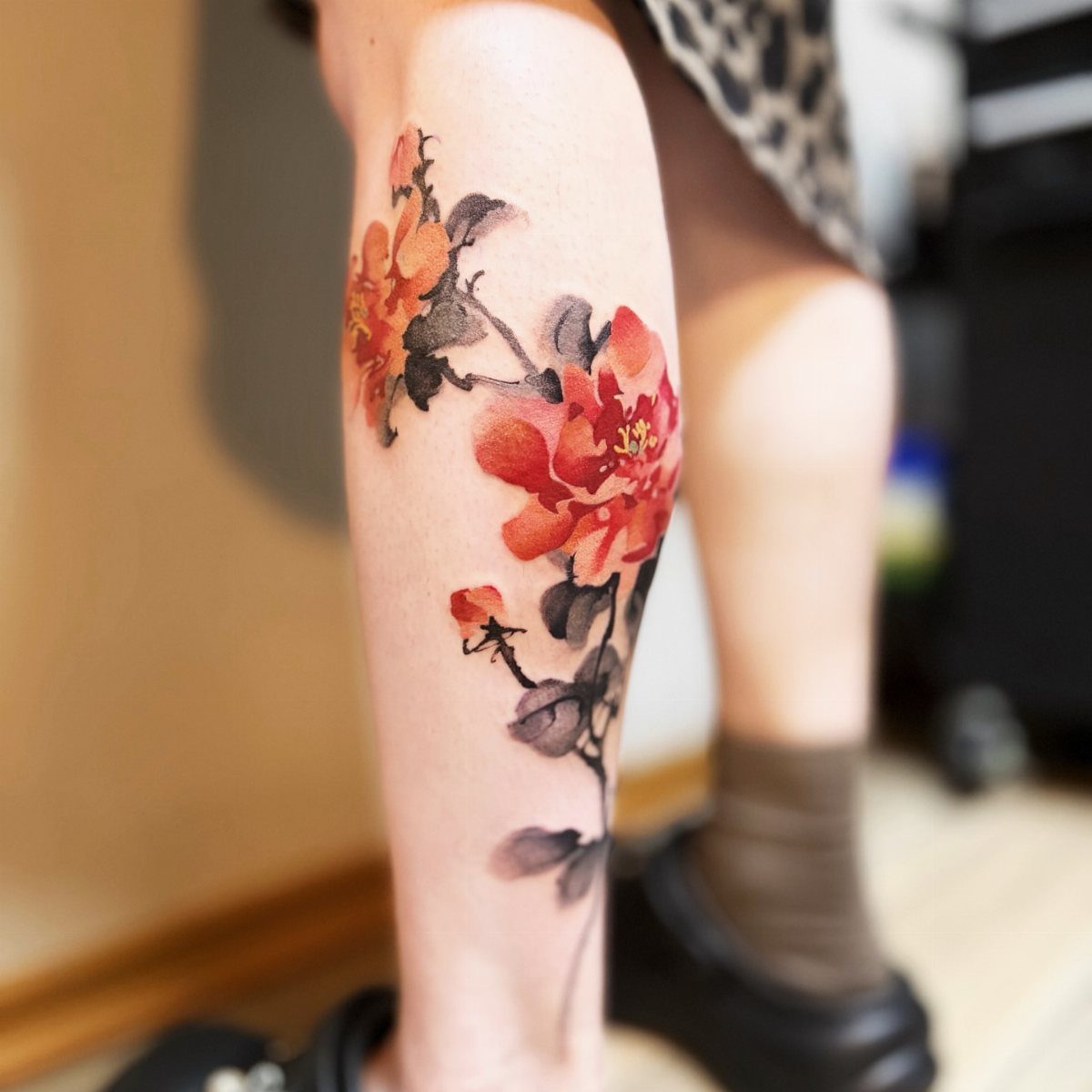 Watercolor tattoo of red flowers on a person's lower leg