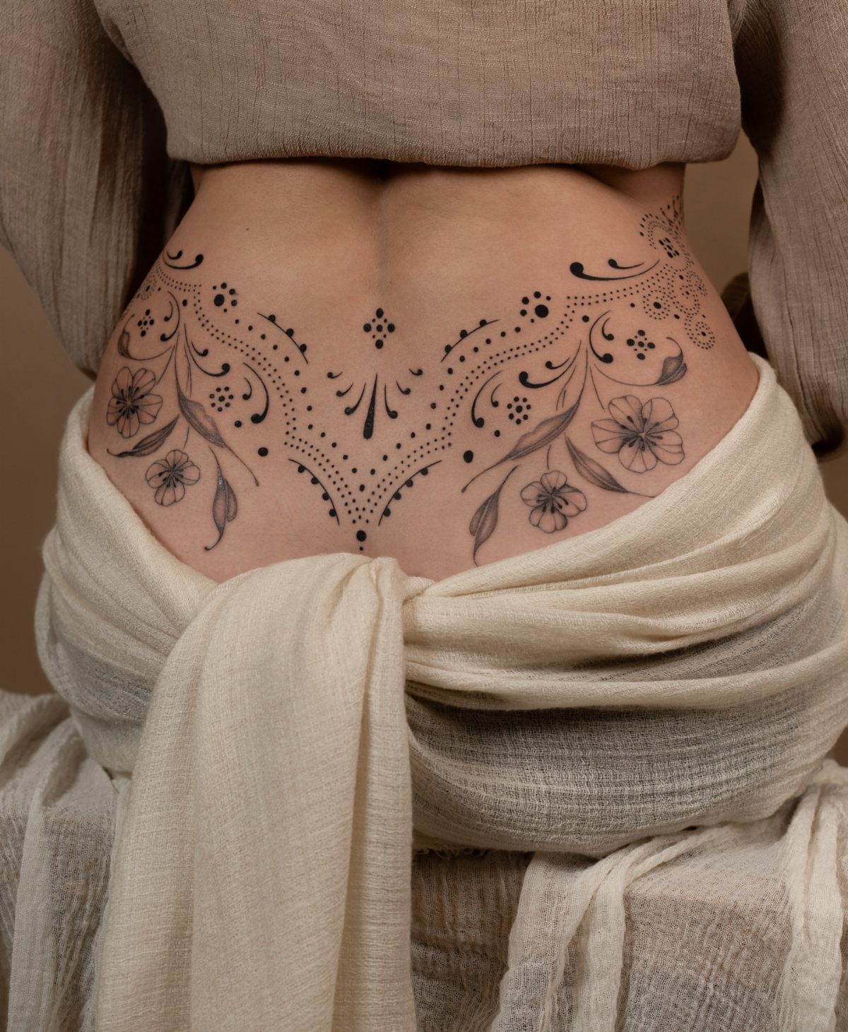 Symmetrical black ink floral and abstract tattoo on a person's lower back