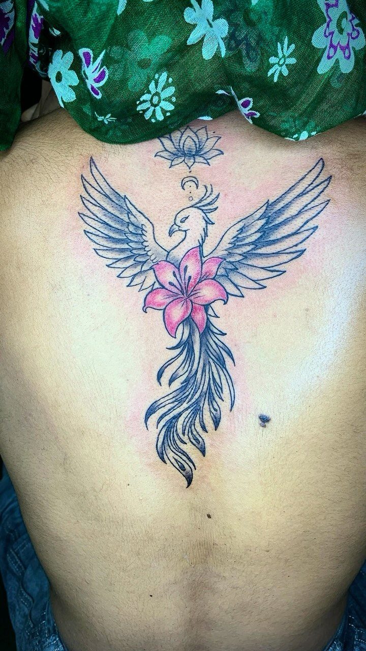 Phoenix tattoo with a pink lily on a person's lower back.