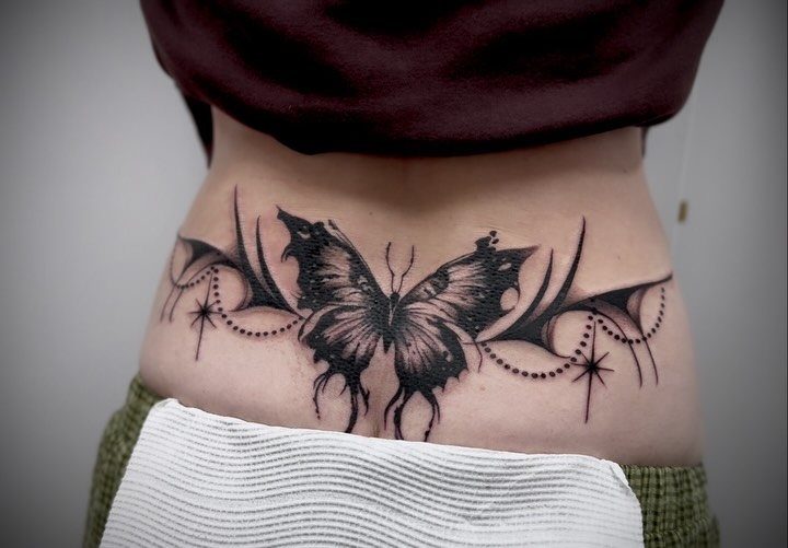 Butterfly tattoo on a lower back with symmetrical wings and decorative star accents.