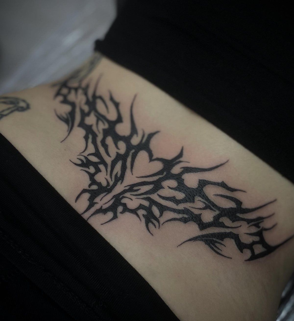 Black ink cyber sigil tattoo on a person's lower back with sharp lines.