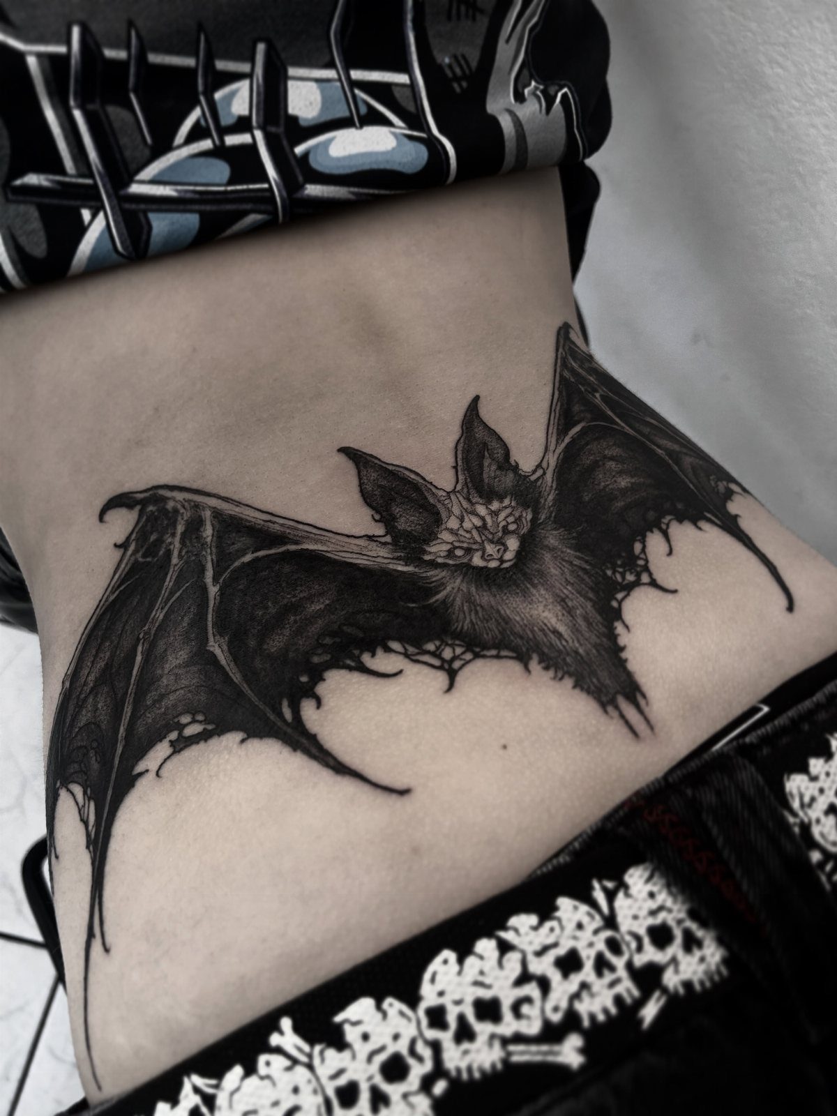 Bat tattoo with outstretched wings on a person's lower back with gothic clothing.