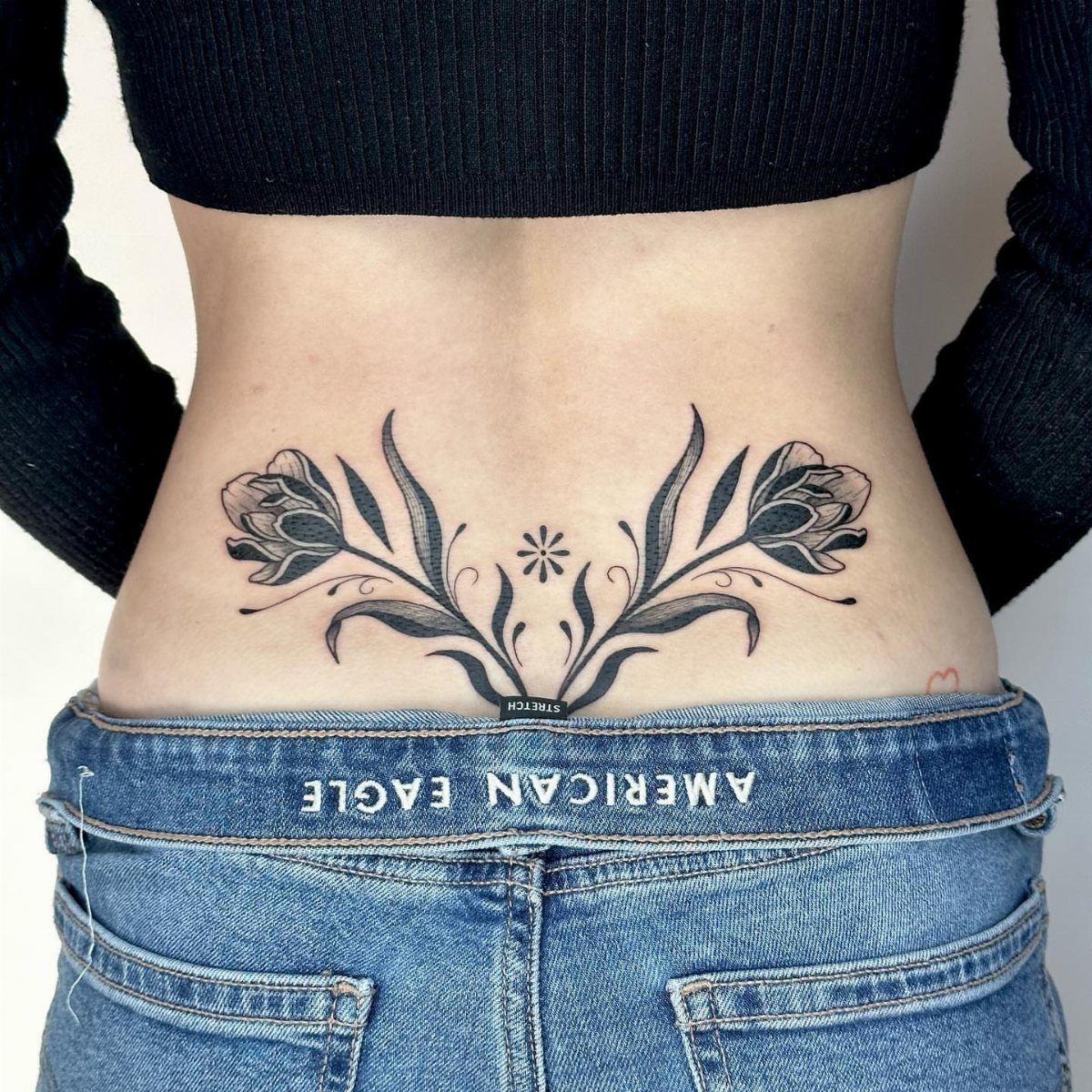 Symmetrical floral lower back tattoo on a person wearing blue jeans and black top