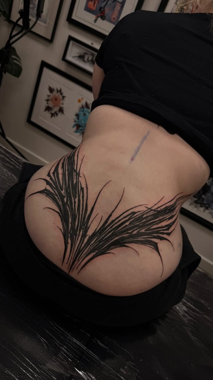 Black neotribal tattoo with sharp tapered lines on a person's lower back.