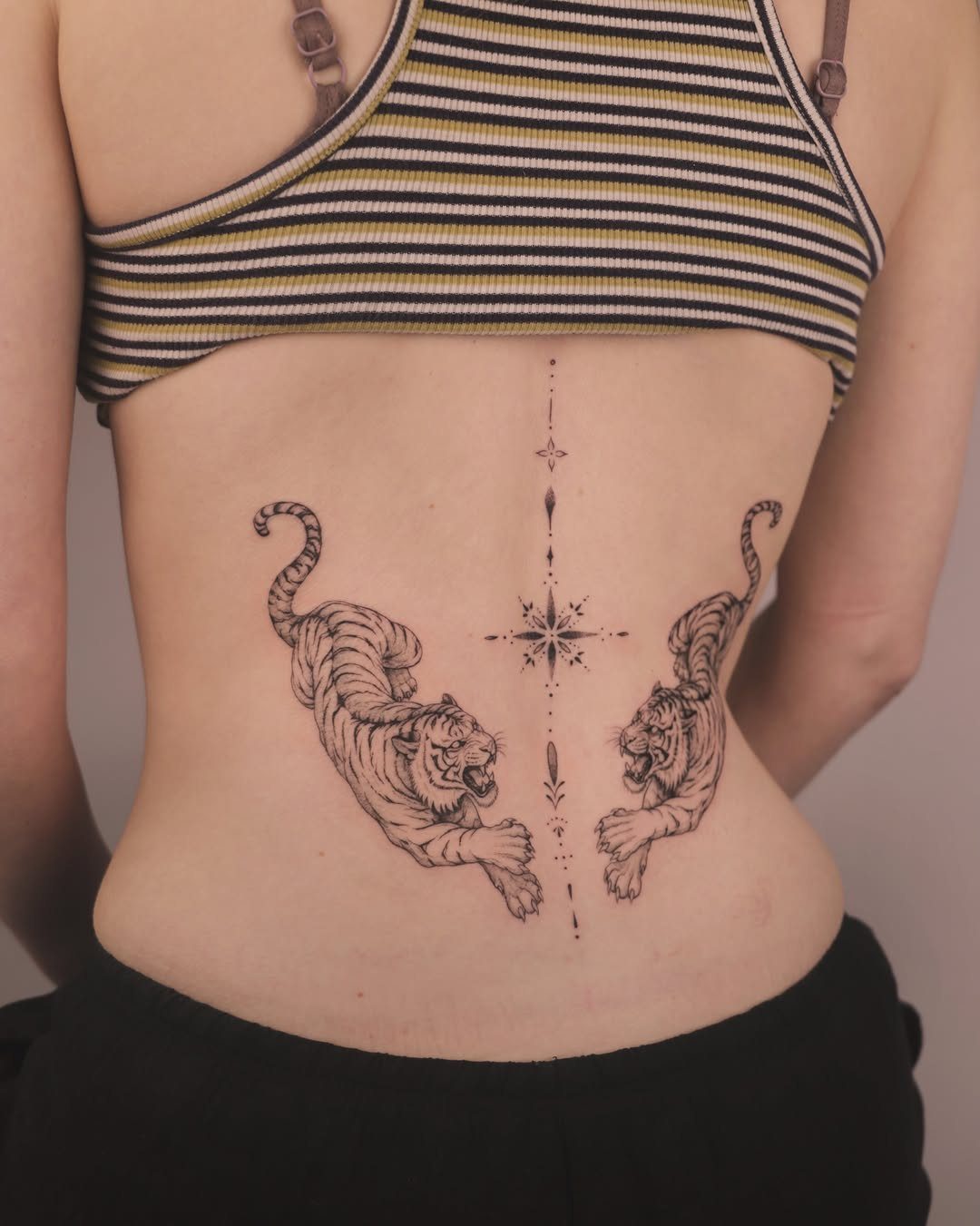 Symmetrical tiger tattoos on a person's lower back with a thin vertical line.