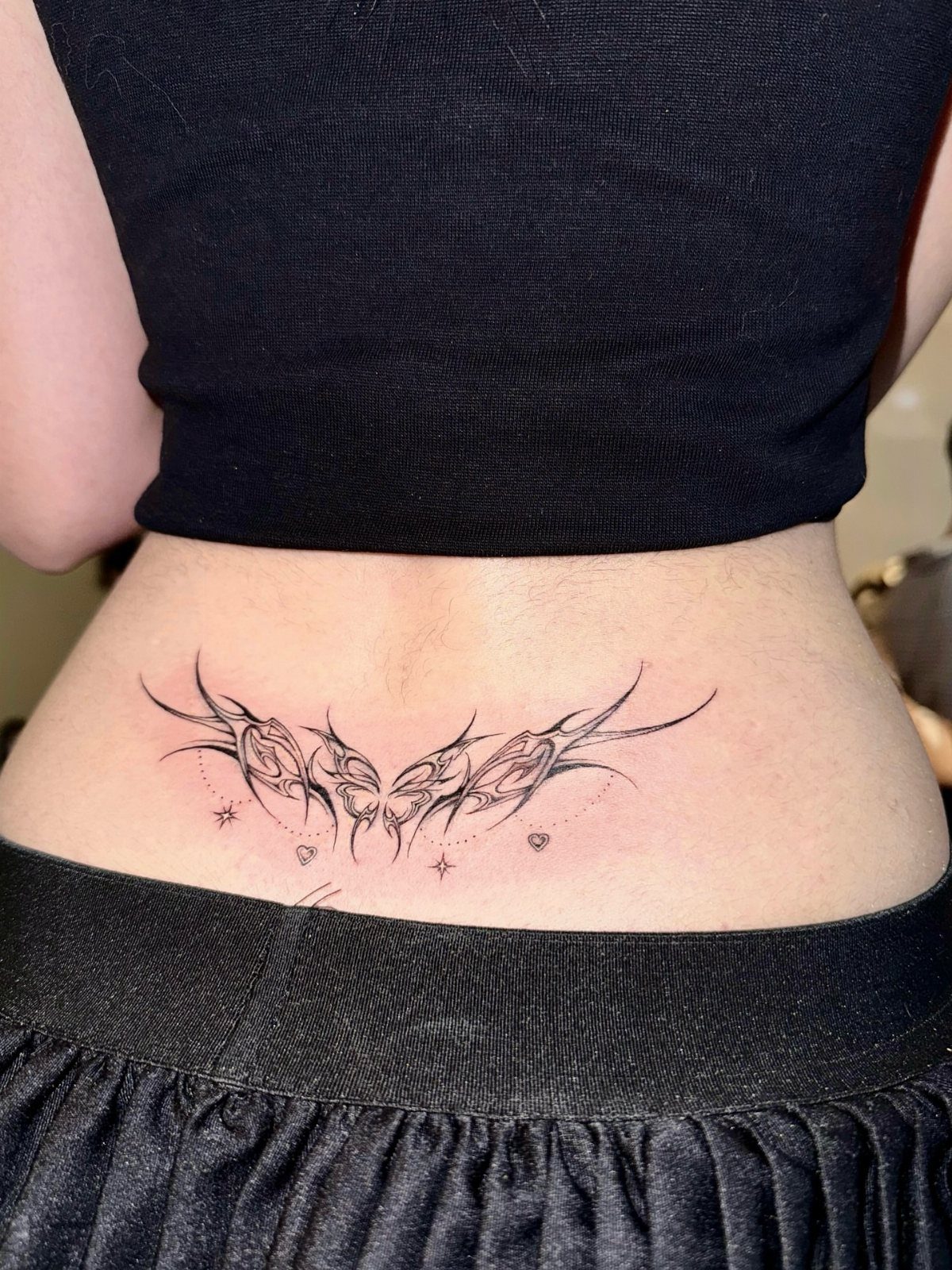 Symmetrical V-shaped tribal tattoo on a person's lower back with small stars.