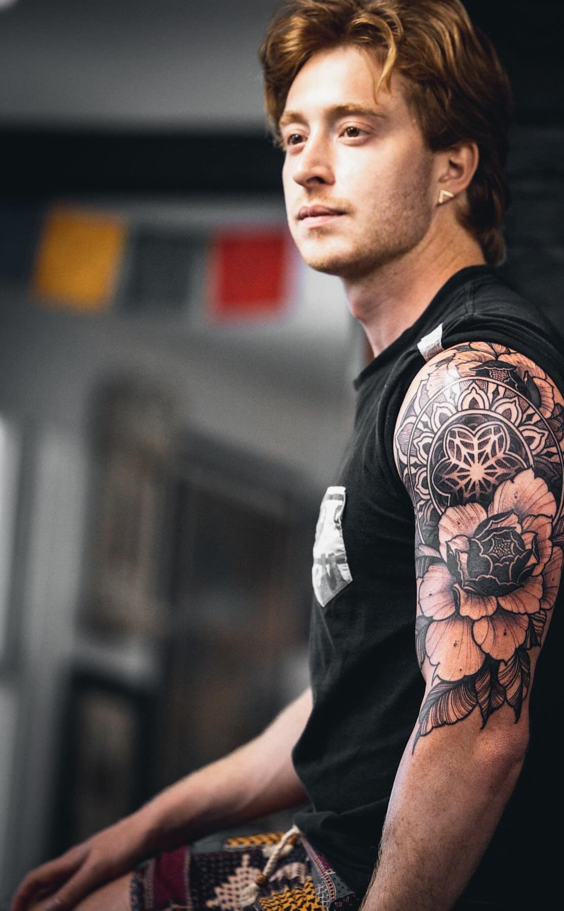 Man with a floral mandala tattoo on his upper arm featuring a peony.