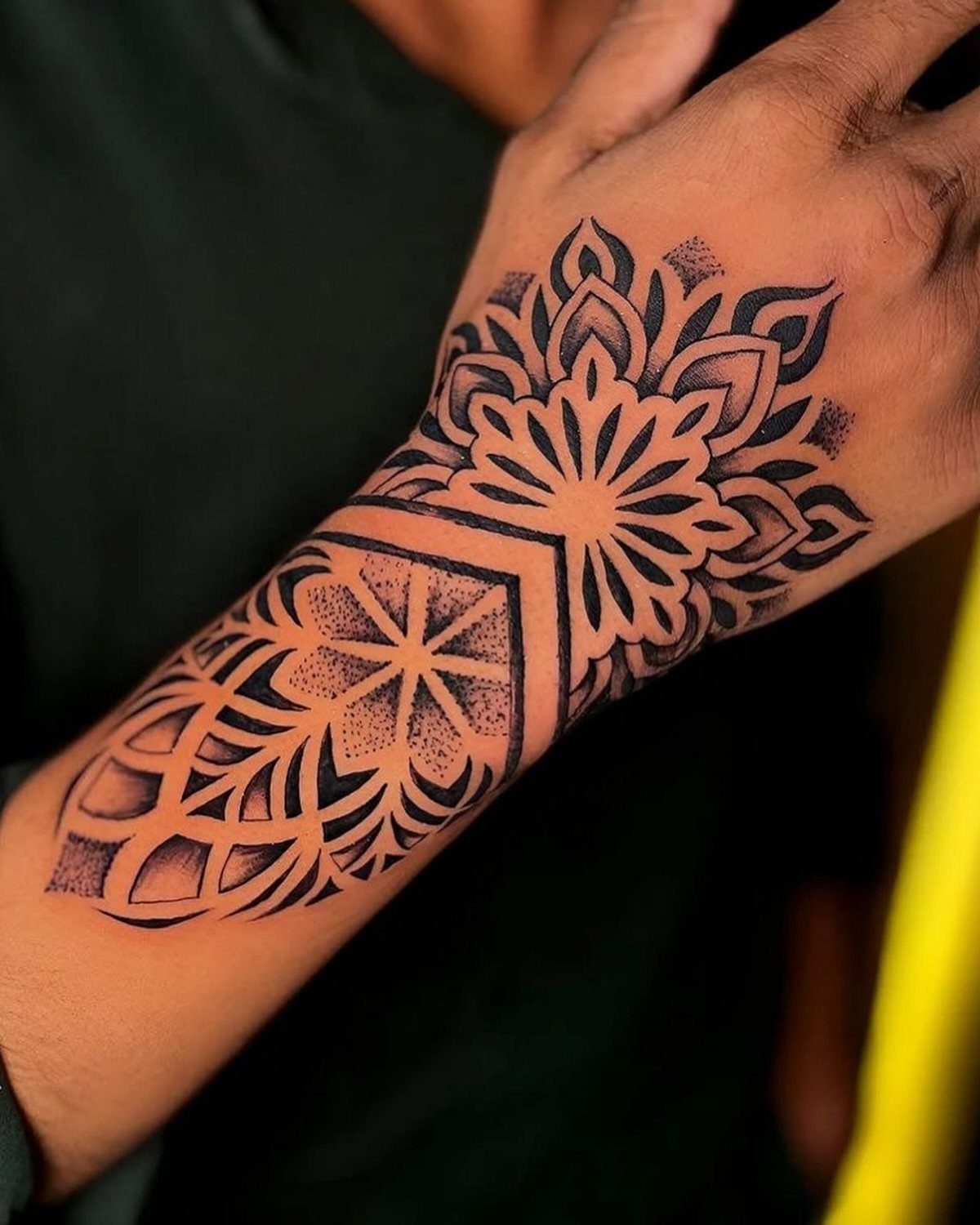 Mandala tattoo on the back of a hand and wrist in black ink
