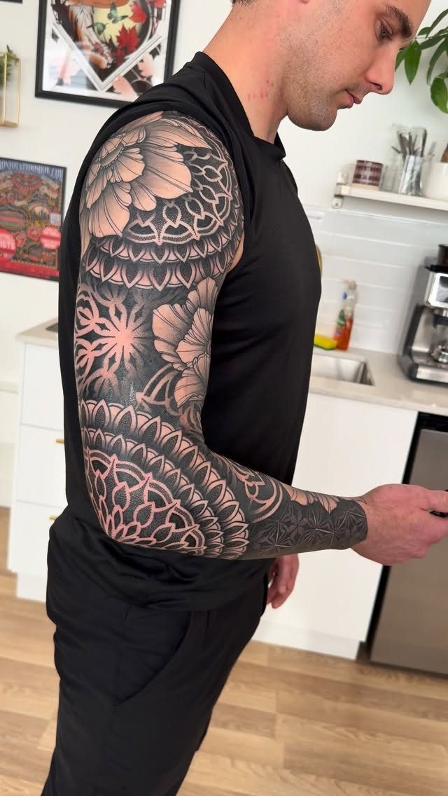Man with a detailed black and grey mandala sleeve tattoo on his arm