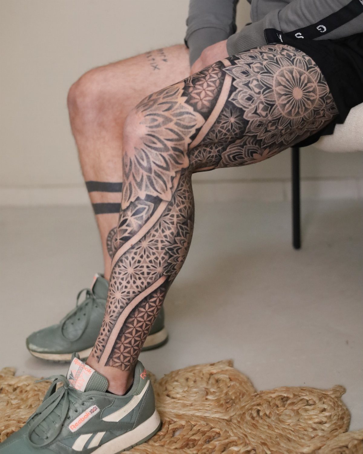 Intricate black ink mandala tattoo covering a man's thigh, knee, and lower leg.