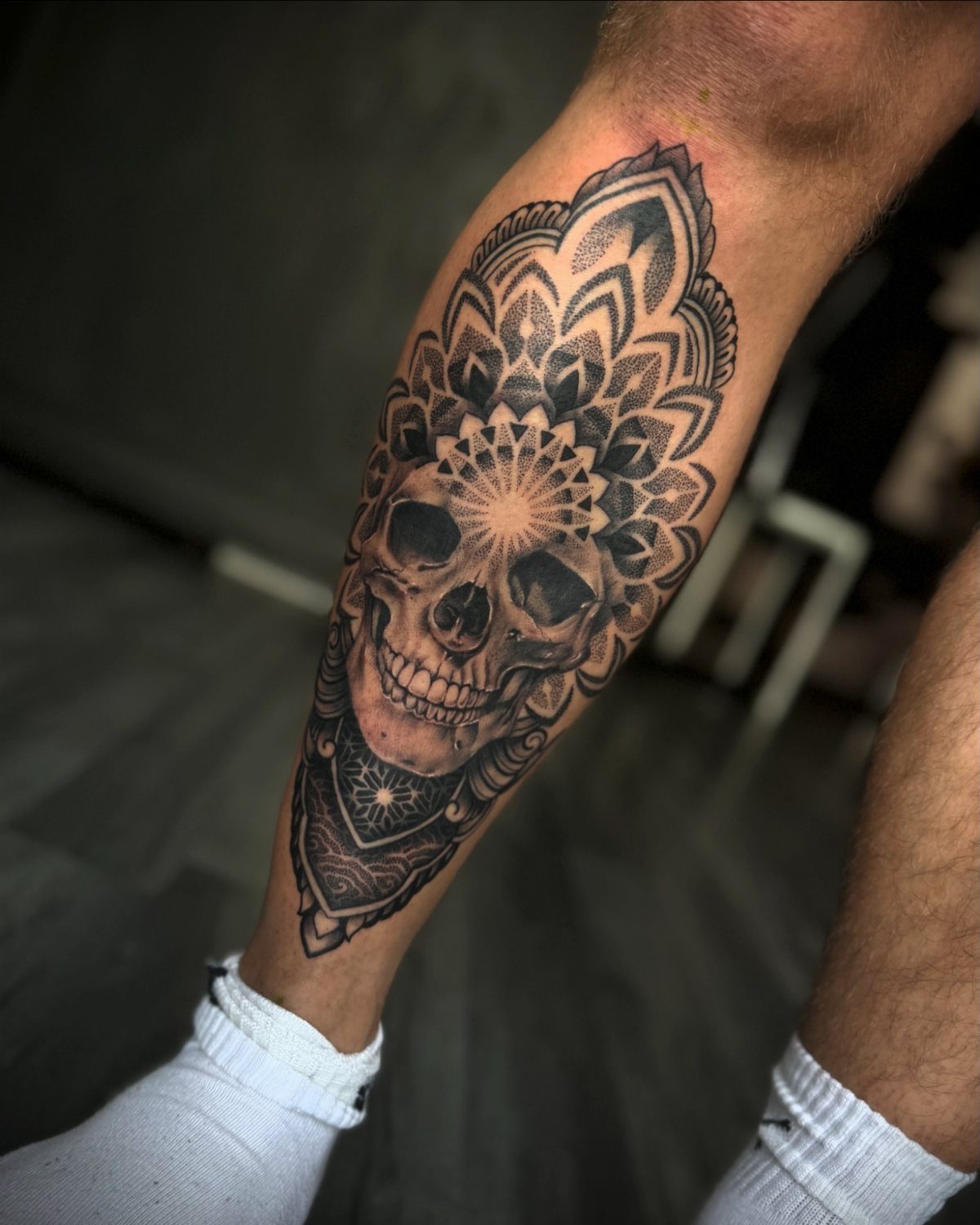 Skull mandala tattoo on a lower leg with intricate geometric patterns and shading.