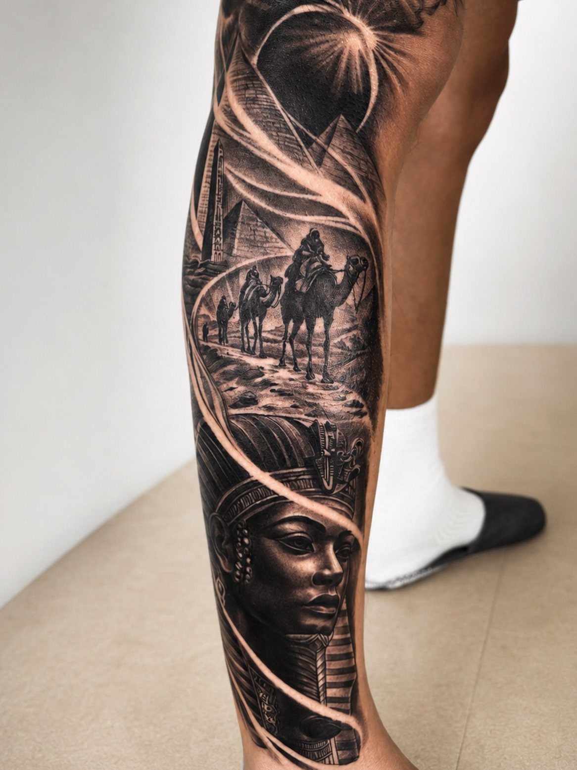 Ancient Egypt leg tattoo featuring a pharaoh, pyramids, and camels in black and grey.