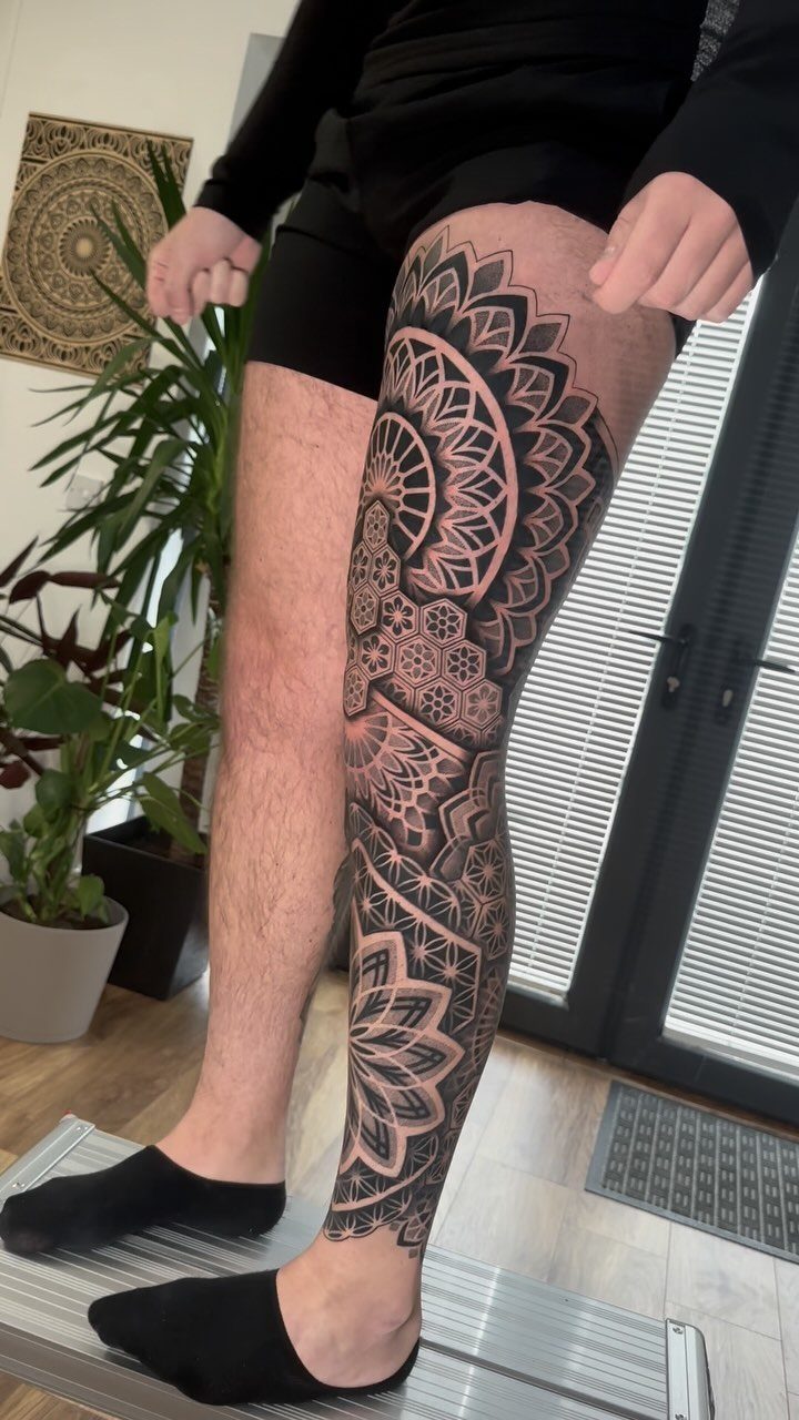 Man's leg with a full sleeve geometric mandala tattoo in black ink