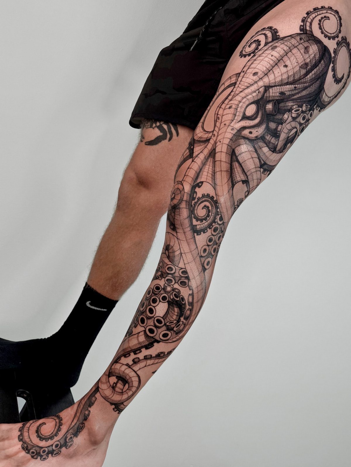 Kraken tattoo with detailed tentacles wrapping around a man's leg from thigh to ankle.