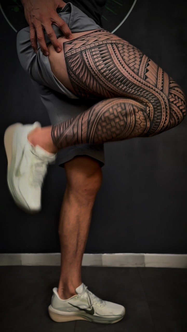 Man's leg with a detailed black tribal Polynesian tattoo and white sneakers.
