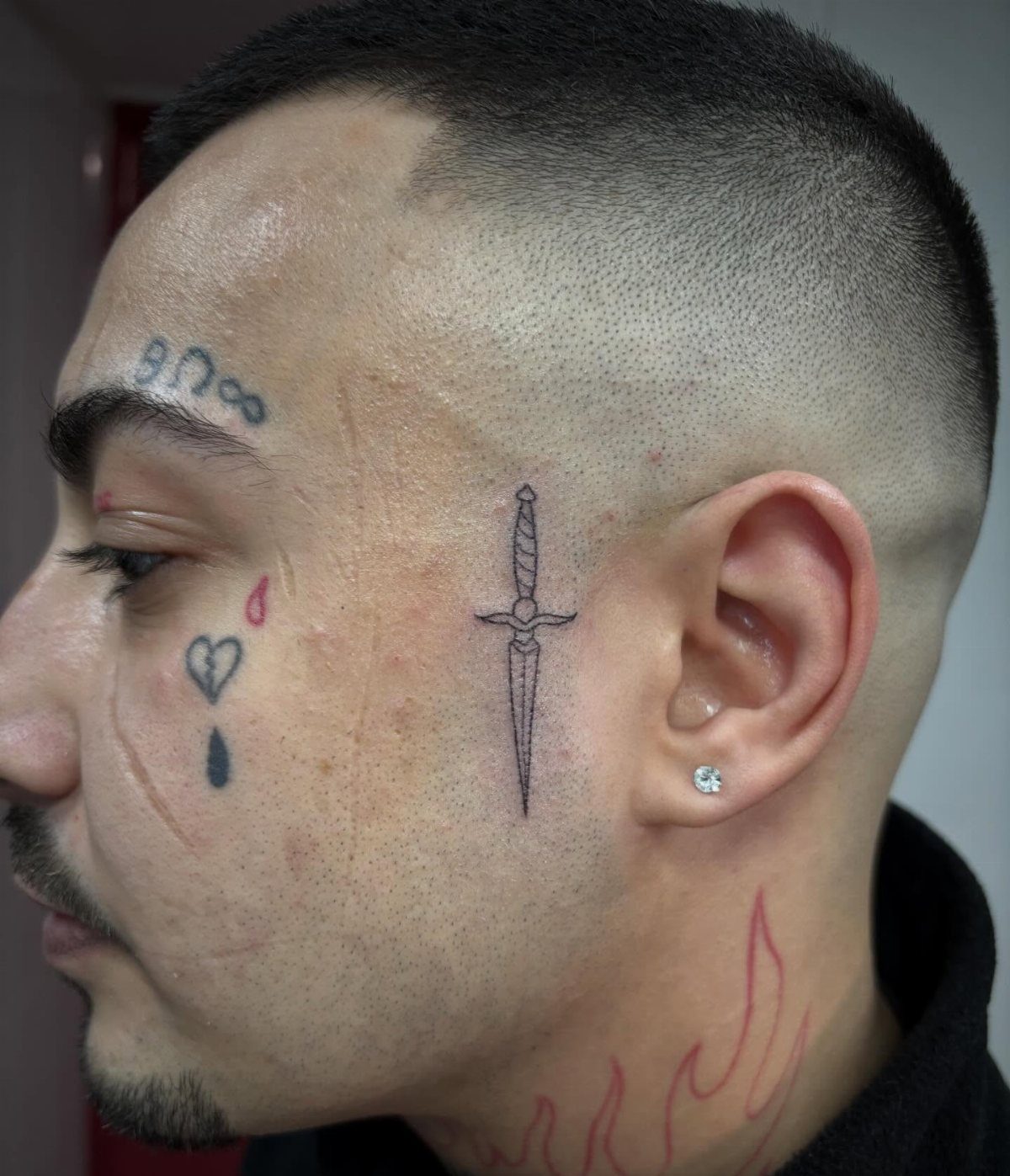 Man's face profile with a dagger tattoo on the cheek and other facial ink.