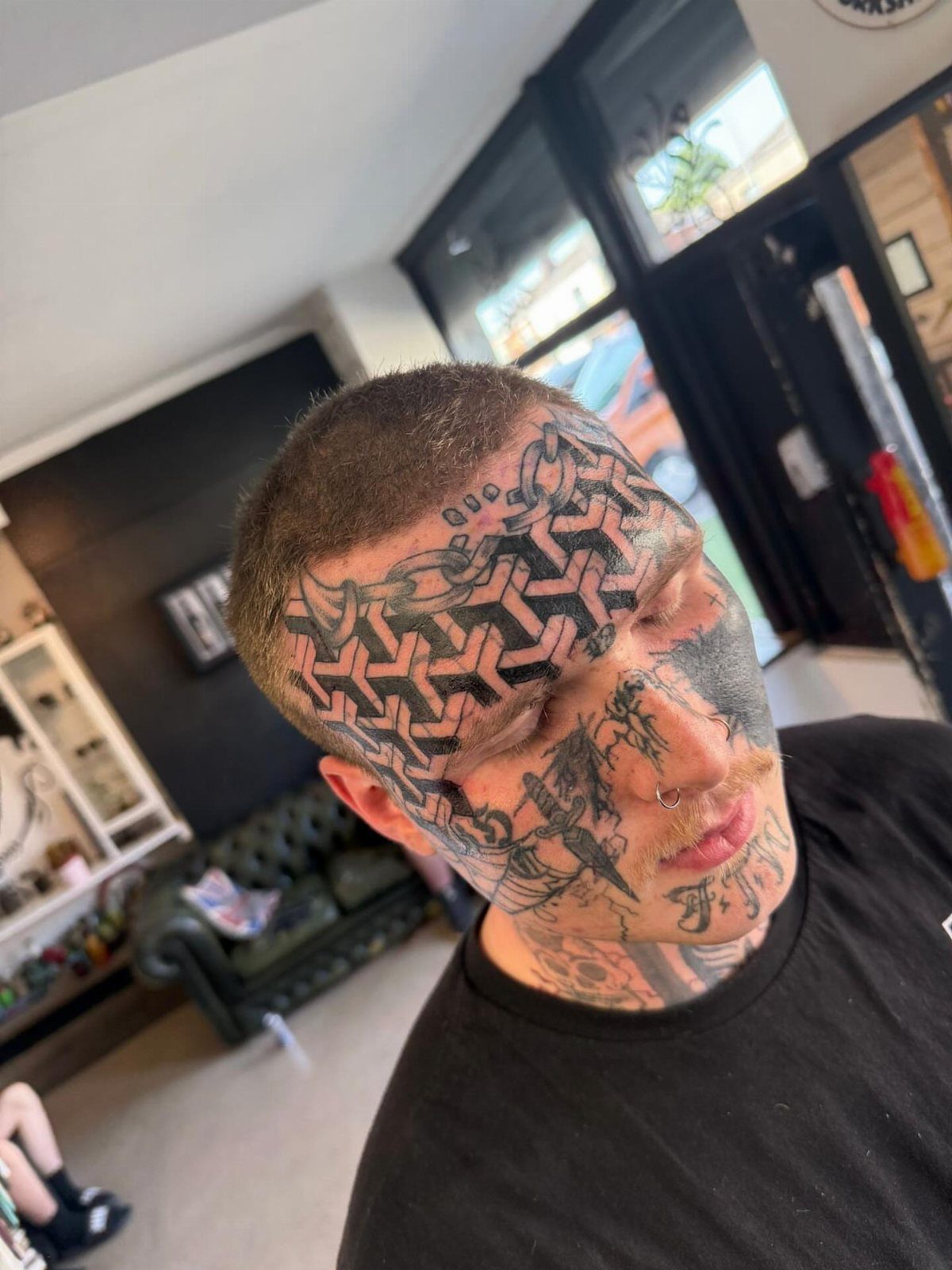 Man with complex geometric line art and illustrative tattoos covering his face and neck.