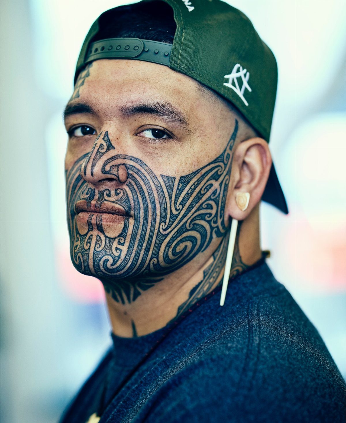 Man with traditional Māori Ta Moko facial tattoos wearing a green baseball cap.