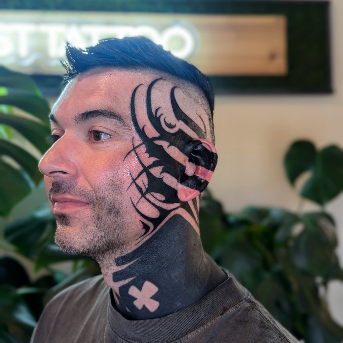 Man with bold black tribal tattoos on his face, ear, and neck.