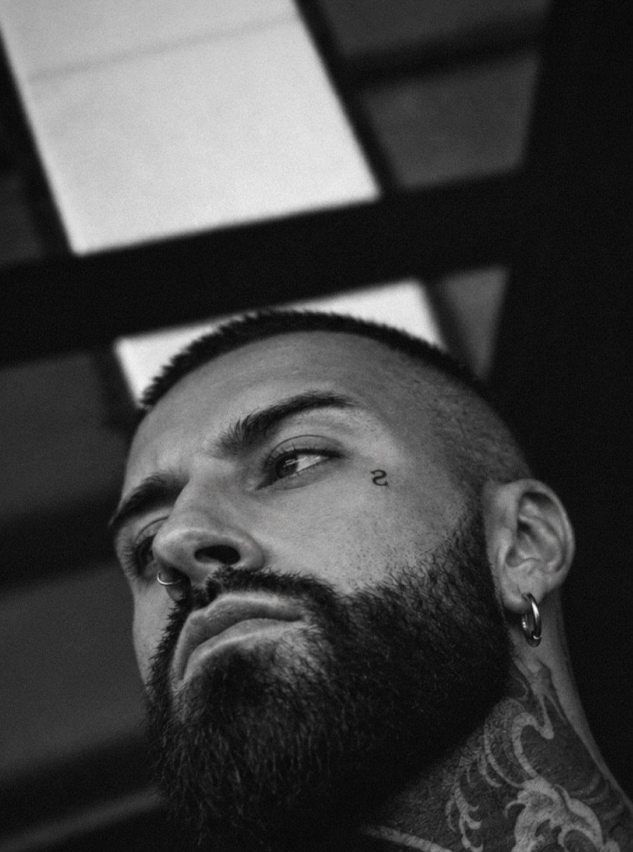 Man with a full beard and small facial tattoos looking upwards in black and white.