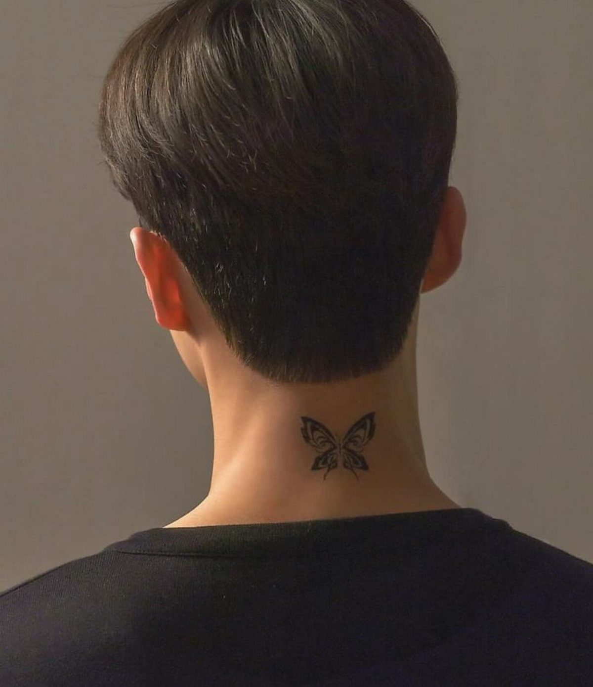 Small black butterfly tattoo on the back of a man's neck