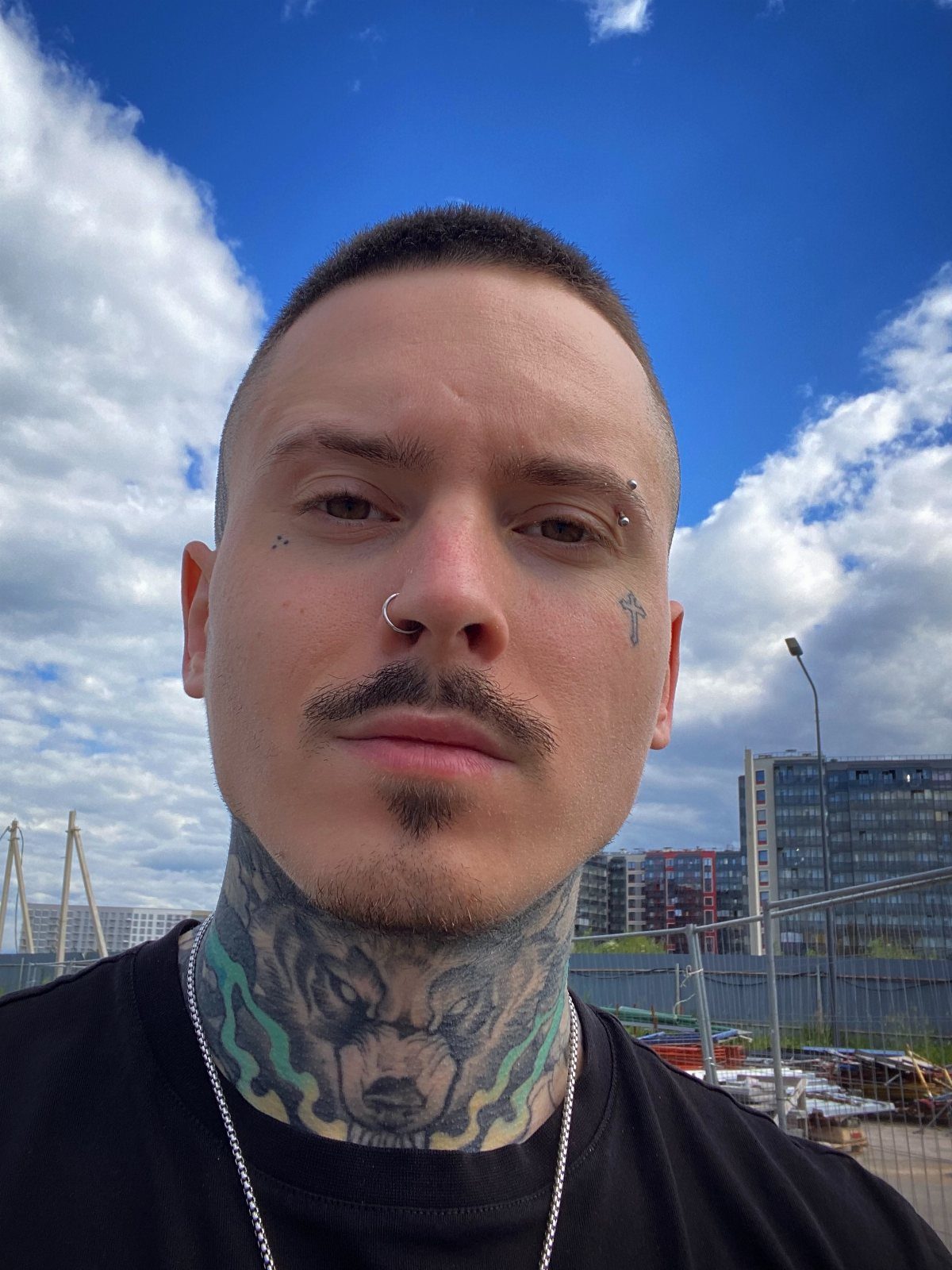 Man with a detailed wolf head tattoo on his neck and facial piercings.