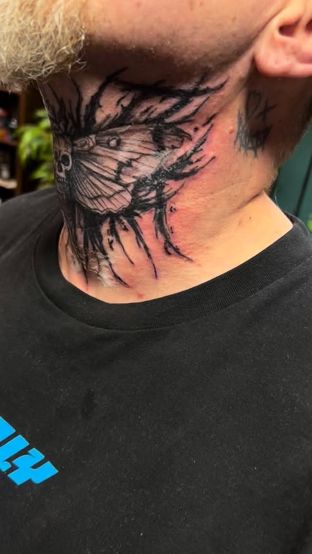 Moth tattoo with abstract black ink splatters on a man's neck.
