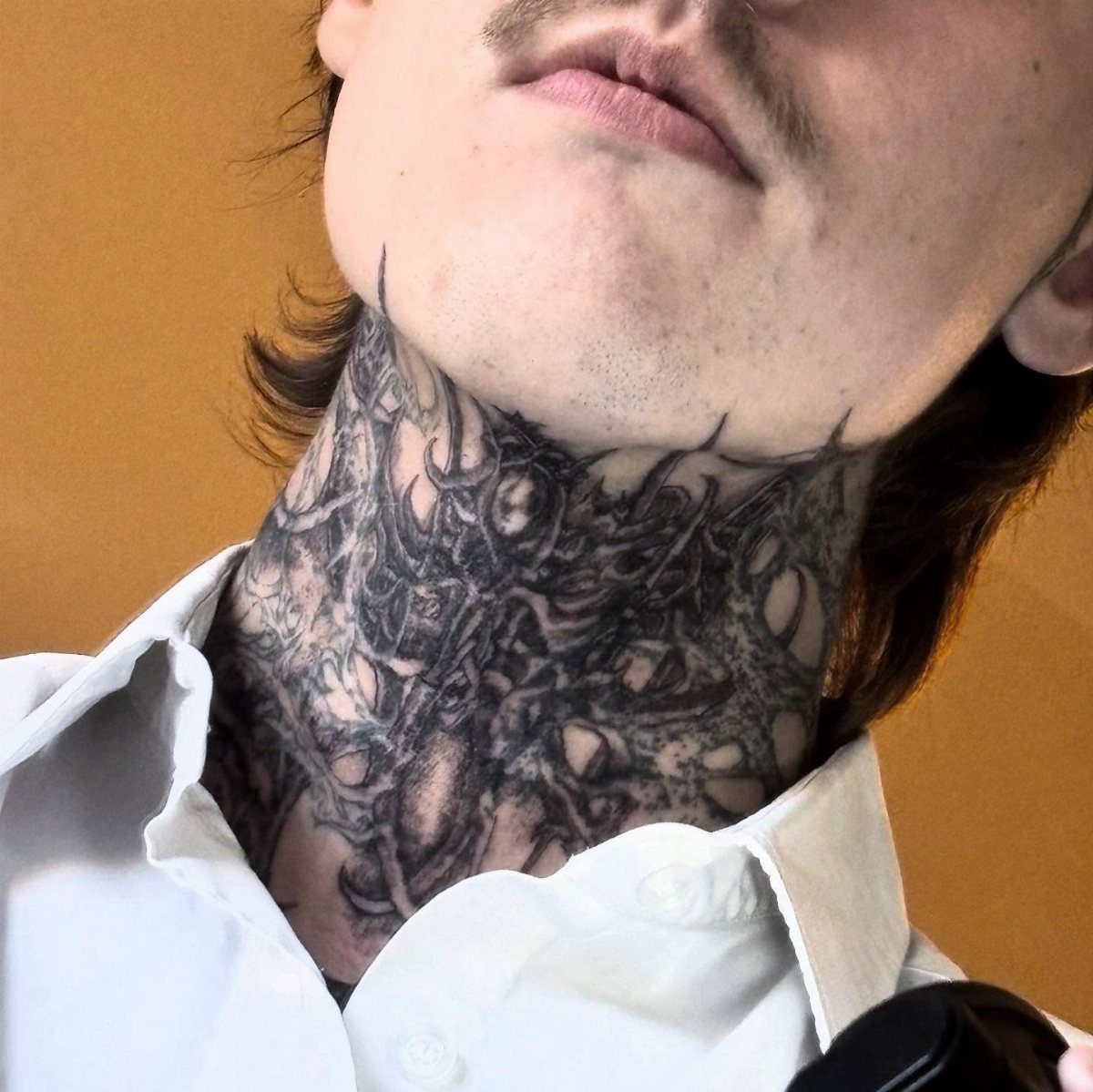 Man with a dense black organic pattern tattoo covering his entire neck.