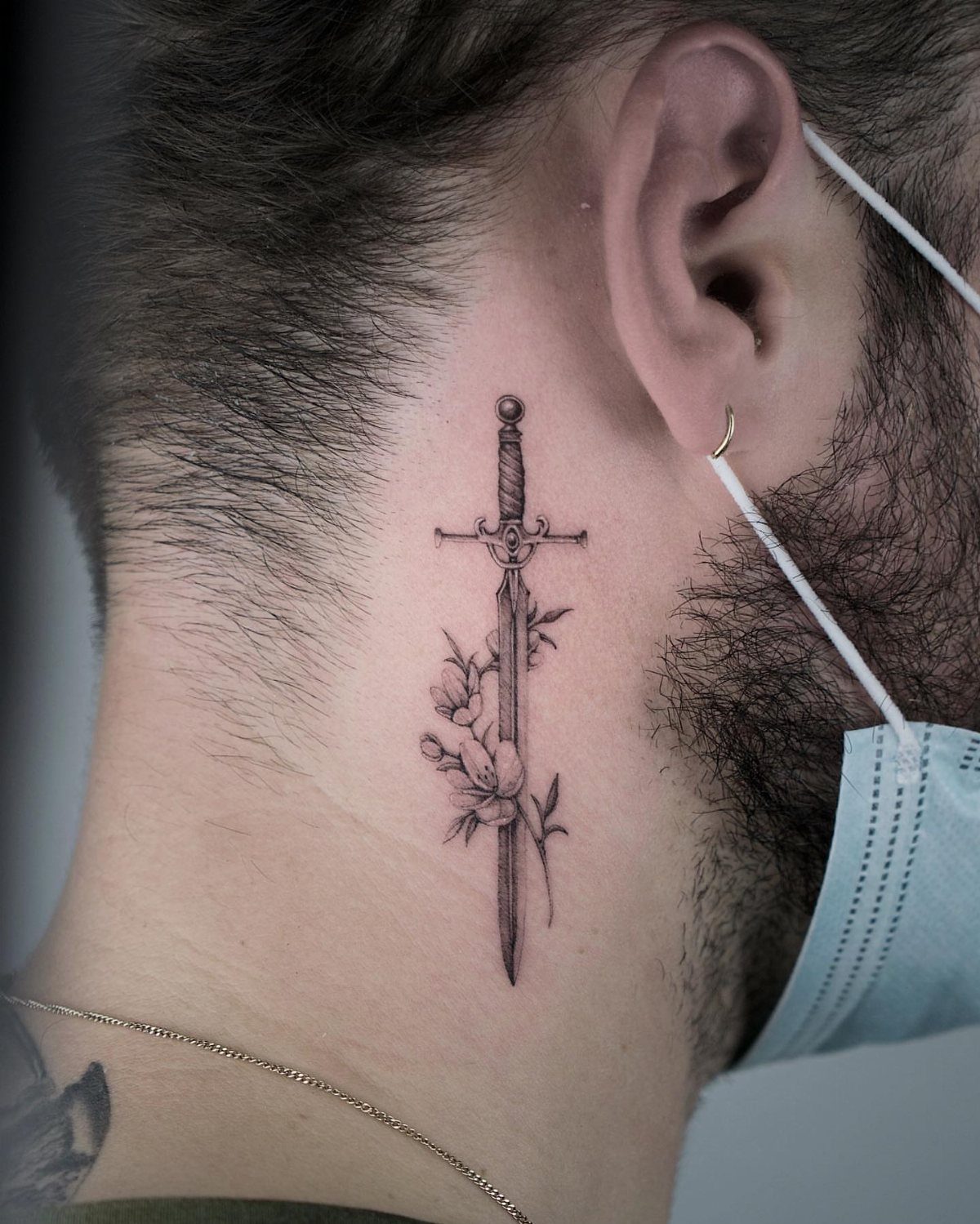 Sword and flower tattoo on the side of a man's neck
