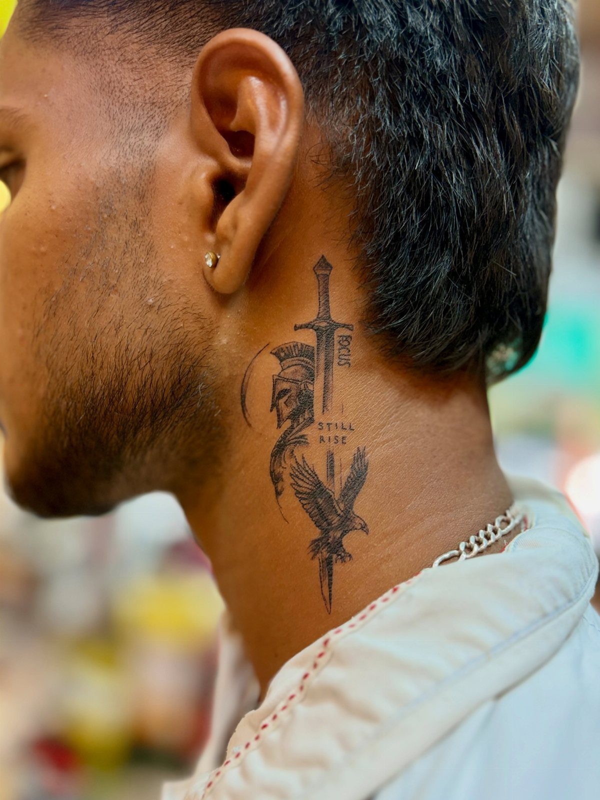 Man's neck tattoo featuring a vertical sword, a helmet, and a bird.